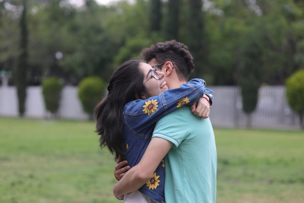 A joyful young couple shares an affectionate hug outdoors in a green park.