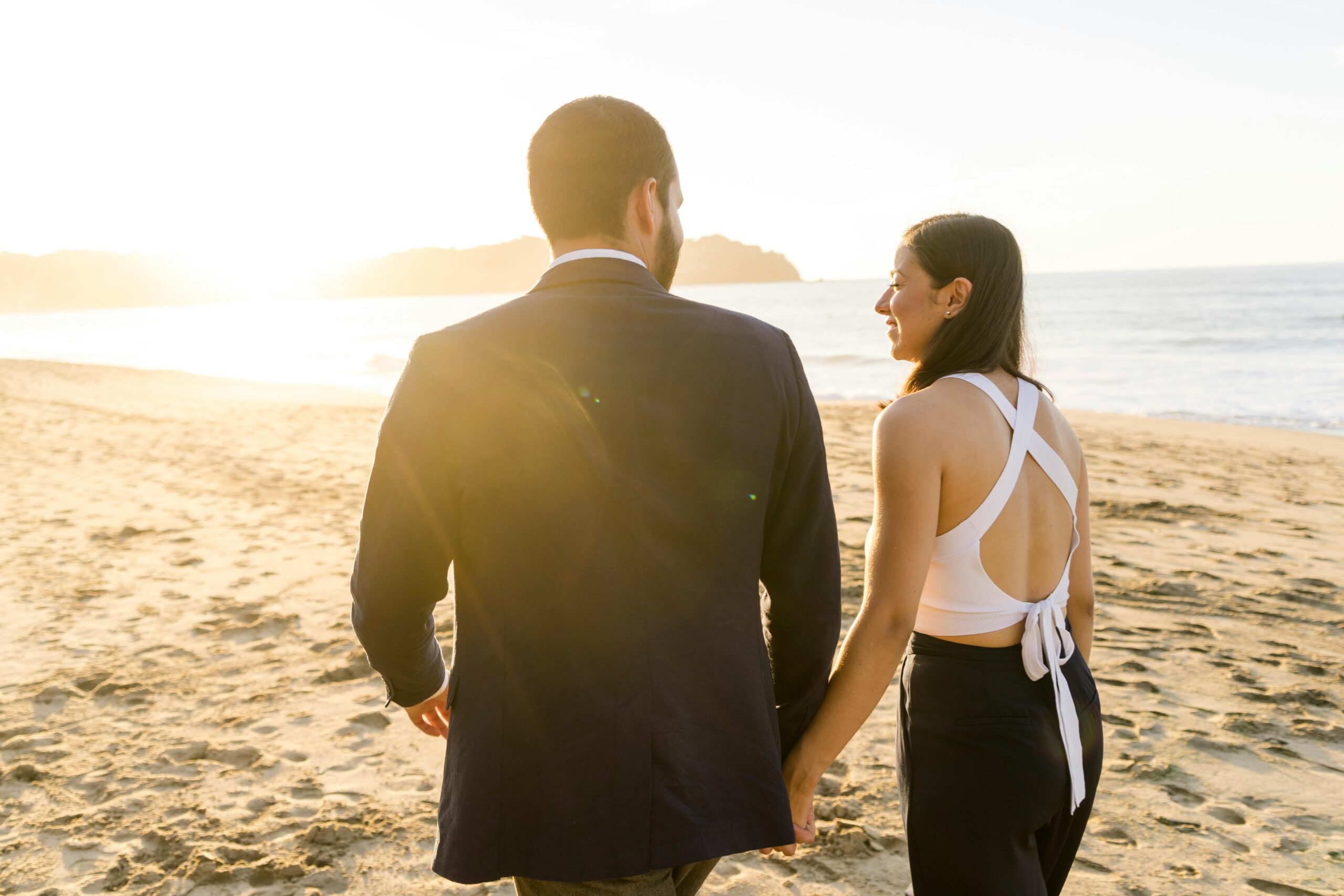 A couple walks hand in hand on a sunlit beach, capturing a romantic sunset moment.