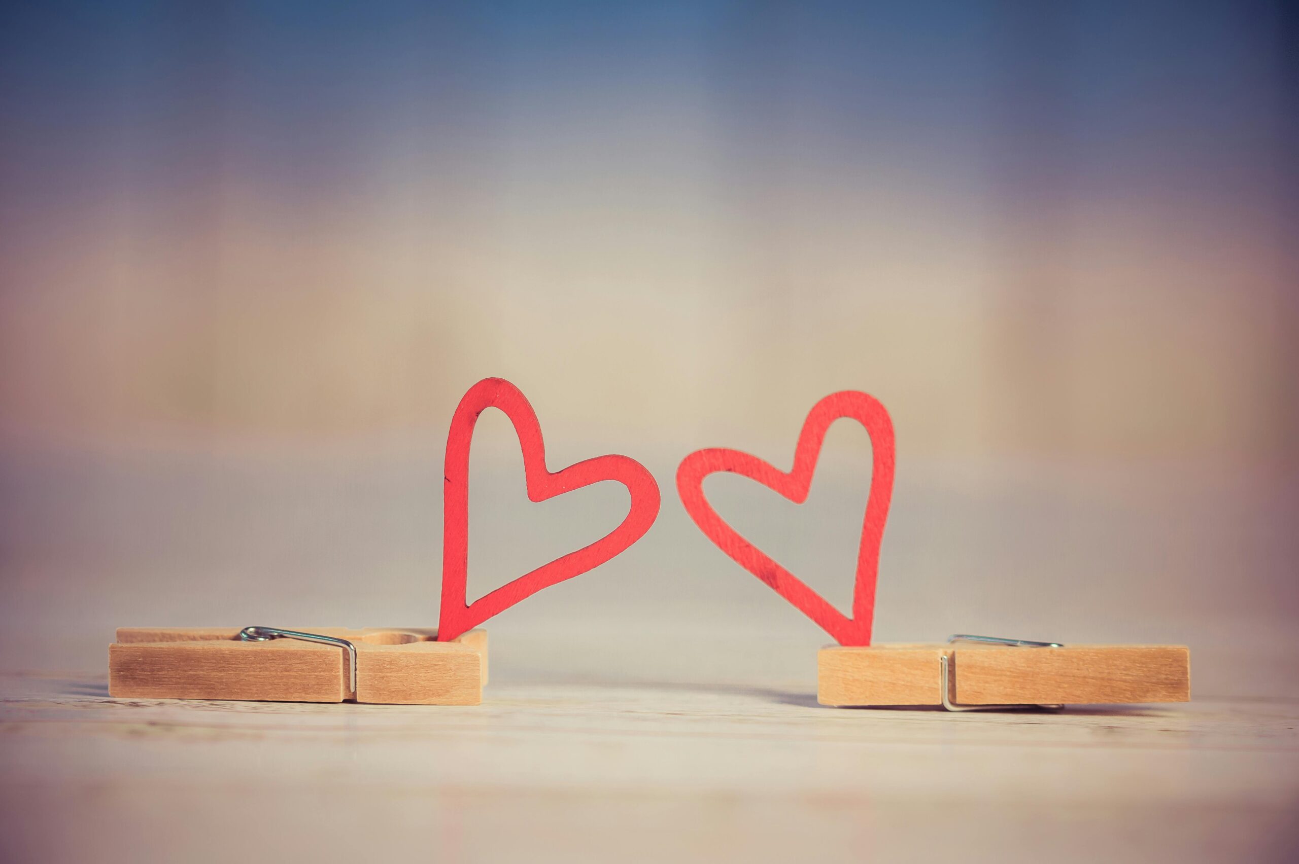 Two wooden clothespins with red heart shapes, symbolizing love and romance, on a blurred background.